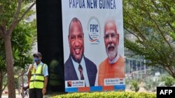 একজন নিরাপত্তা কর্মী একটি ব্যানারের পাশে দাঁড়িয়ে আছেন। তাতে পাপুয়া নিউ গিনির প্রধানমন্ত্রী (বামে) এবং ভারতের প্রধানমন্ত্রীর ছবি দেখা যাচ্ছে। পোর্ট মোরেসবি, ১৮মে, ২০২৩।