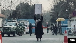 FILE - A young woman protests alone against a Taliban ban on women's higher education, outside Kabul University, as Taliban guards stand by, in Kabul, Afghanistan, Dec. 25, 2022. 