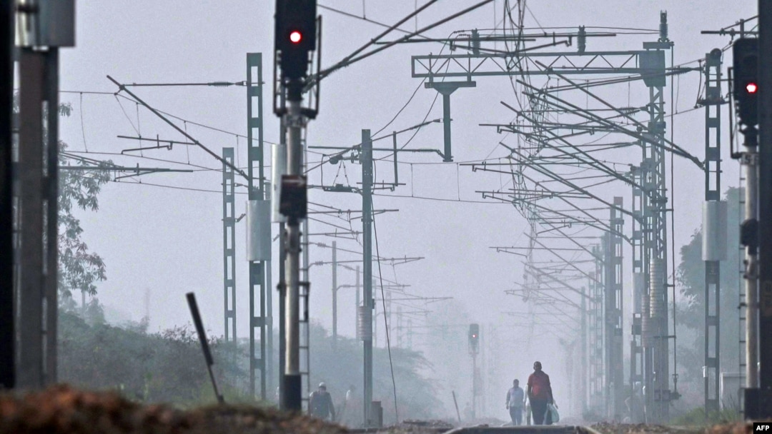 People walk through railway tracks amid smoggy conditions on the outskirts of New Delhi, India, Oct. 30, 2023.