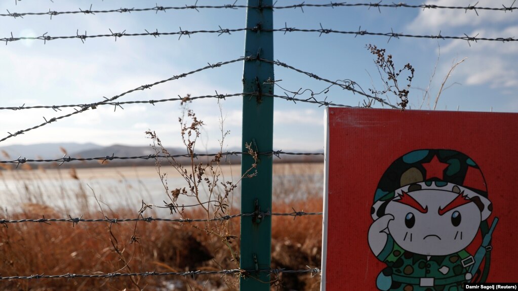 资料图片：2017年11月24日，在中国珲春市附近，俄罗斯、中国和朝鲜边境的中国一侧，铁丝网上的警示牌上画着一个卡通士兵。（路透社）(photo:VOA)