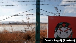 资料图片：2017年11月24日，在中国珲春市附近，俄罗斯、中国和朝鲜边境的中国一侧，铁丝网上的警示牌上画着一个卡通士兵。（路透社）