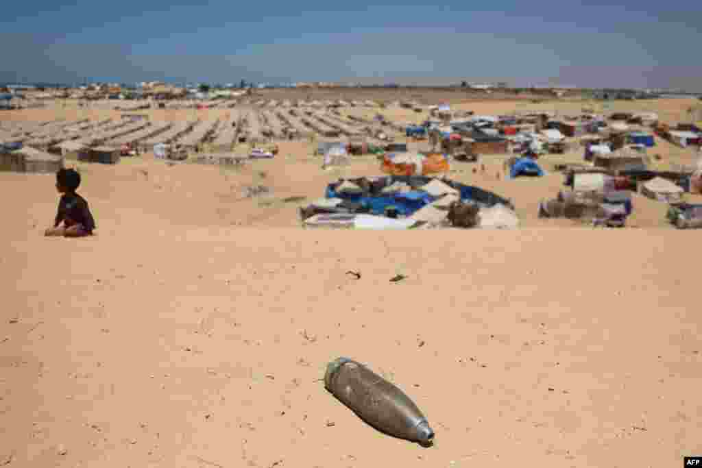 An unexploded shell lies on a sand dune as a young boy sits near a makeshift camp for displaced Palestinians in the area of Tel al-Sultan in Rafah in the southern Gaza Strip.
