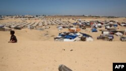 An unexploded shell lies on a sand dune as a young boy sits near a makeshift camp for displaced Palestinians in the area of Tel al-Sultan in Rafah in the southern Gaza Strip.