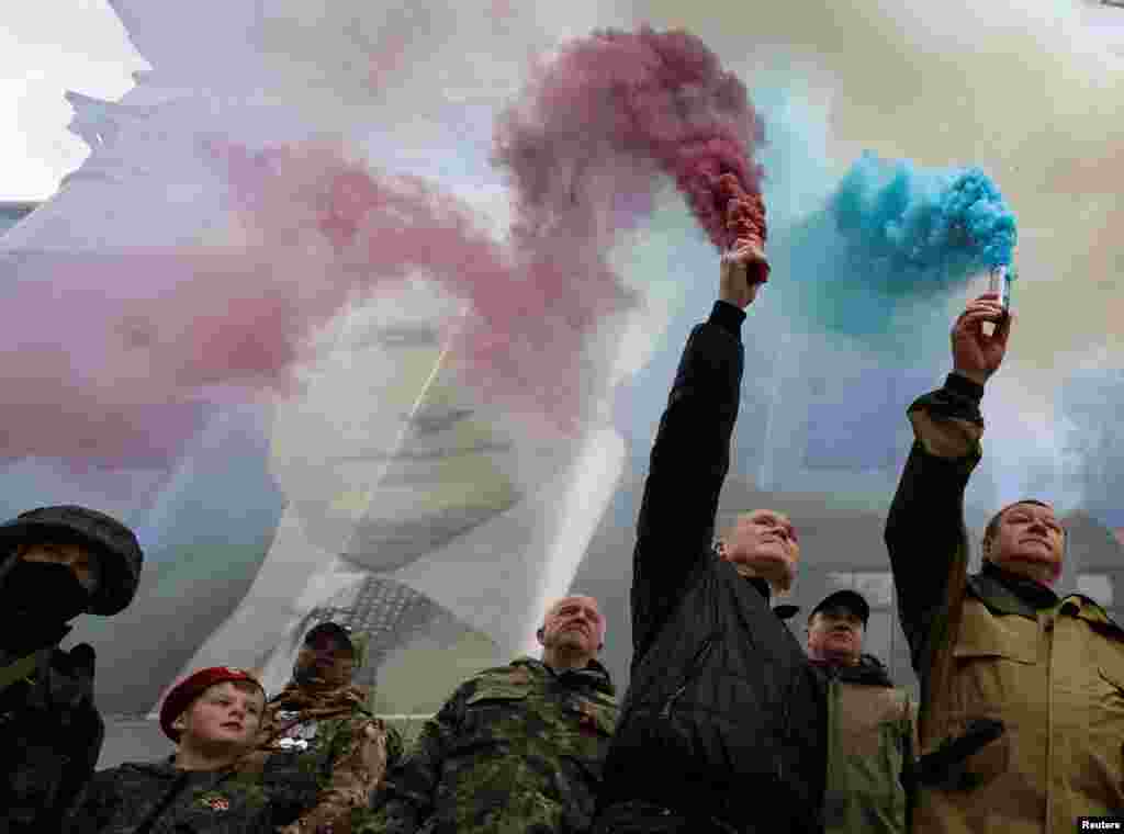 Participants burn flares in front of a banner with a portrait of Russian President Vladimir Putin during a patriotic flash mob marking the ninth anniversary of Russia's annexation of Crimea, in Yalta, Crimea.