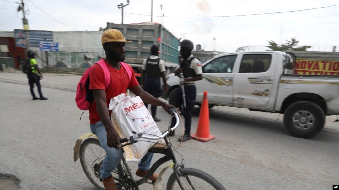A man cycles past police officers on patrol near the airport, in Port-au-Prince, Haiti, June 1, 2024. 