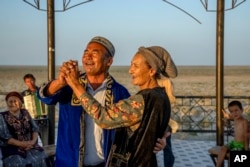 A man and woman dance next to a sand lot filled with ships formerly used on the Aral Sea, in Muynak, Uzbekistan, July 11, 2023.