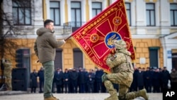El presidente de Ucrania, Volodymyr Zelenskyy, sostiene la bandera de una unidad militar mientras un oficial la besa durante un evento conmemorativo con motivo del primer aniversario de la guerra entre Rusia y Ucrania en Kiev, Ucrania, el 24 de febrero de 2023.