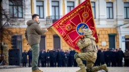 El presidente de Ucrania, Volodymyr Zelenskyy, sostiene la bandera de una unidad militar mientras un oficial la besa durante un evento conmemorativo con motivo del primer aniversario de la guerra entre Rusia y Ucrania en Kiev, Ucrania, el 24 de febrero de 2023.