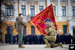 President Volodymyr Zelenskyy holds the flag of a military unit as an officer kisses it on the first anniversary of the Russian invasion of Ukraine, in Kyiv, Feb. 24, 2023.