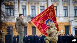Presiden Ukraina Volodymyr Zelenskyy memegang bendera unit militer ketika seorang perwira menciumnya pada acara peringatan satu tahun perang Rusia-Ukraina di Kyiv, Ukraina, 24 Februari 2023.