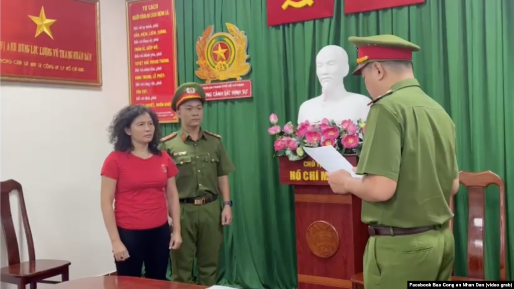 Nhà báo Hàn Ni (áo đỏ) nghe một viên chức công an đọc quyết định bắt tạm giam, khởi tố bà về cáo buộc lợi dụng các quyền tự do dân chủ, tại Thành phố Hồ Chí Minh, ngày 24 tháng 2, 2023.