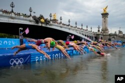 Athletes dive into the water for the start of the women's individual triathlon competition at the 2024 Summer Olympics, July 31, 2024, in Paris, France.