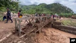 People walk across a bridge strewn with flood debris in western Rwanda, May 3, 2023.