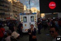 An ambulance passes next to people who are gathering to watch a concert after the welcoming ceremony of the Belem, the three-masted sailing ship which is carrying the Olympic flame, at the Old Port in Marseille, southern France, May 8, 2024.