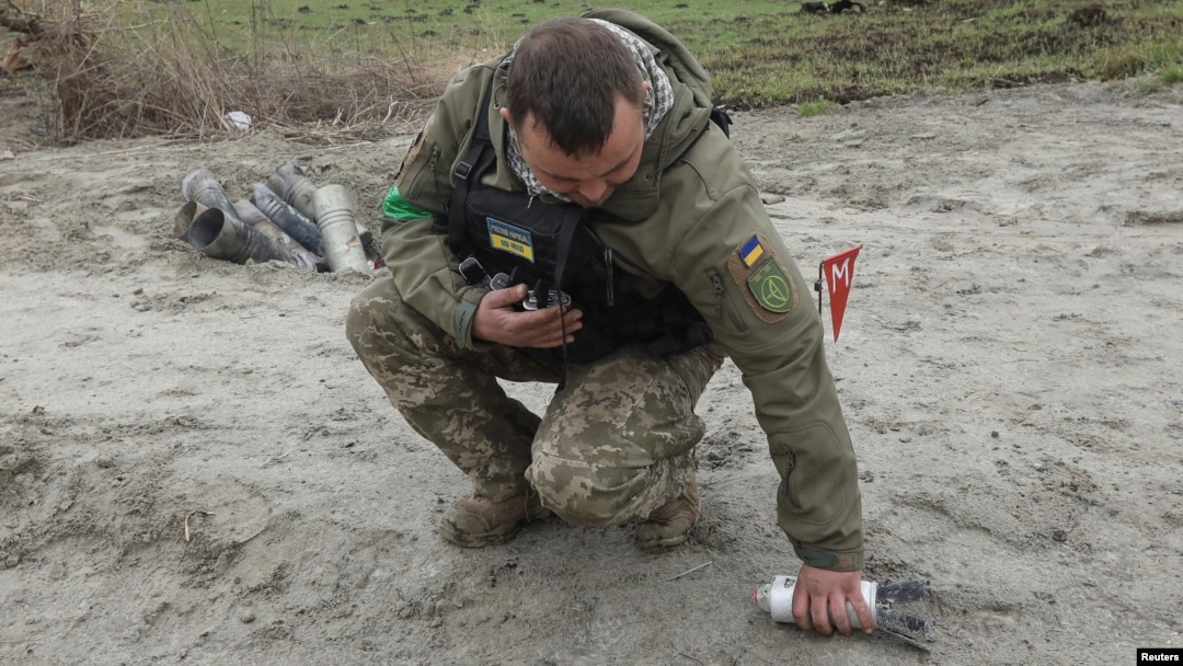 Seorang tentara pencari ranjau tampak mengambil serpihan bom tandan yang gagal meledak di area dekat desa Motyzhyn, di Kyiv, Ukraina, pada 10 April 2022. (Foto: Reuters/Mykola Tymchenko)