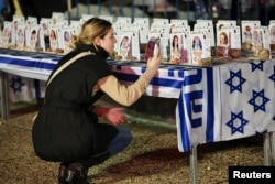 A person takes a picture of images of Israeli hostages who are being held in the Gaza Strip after they were seized by Hamas gunmen on October 7, displayed at a table with the colors of the Israeli flag, in Tel Aviv, Israel, Dec. 12, 2023.