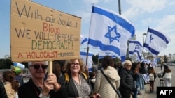 Israeli protesters lift national flags and placards as they rally in Tel Aviv on Feb. 13, 2023, against controversial legal reforms being touted by the country's hard-right government.