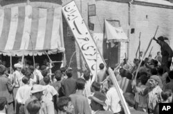 Sekelompok demonstran merobek papan nama Partai Iran dari depan markas besar di Teheran pada 19 Agustus 1953, selama kudeta yang didukung CIA yang menggulingkan Perdana Menteri Mohammad Mossadegh dan pemerintahannya. (Foto: AP)