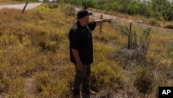 FILE - Jim Hogg County Sheriff's Investigator Ruben Garza investigates the location of a missing water station for immigrants containing sealed jugs of fresh water along a fence line near a roadway in rural Jim Hogg County, Texas, July 25, 2023.