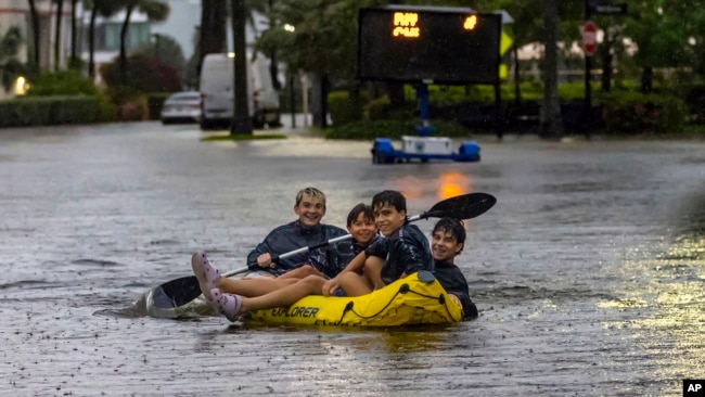 Matthew Koziol, Matías Ricci, Manuel Ricci y Raúl Fernández viajan en balsa por una calle inundada por las fuertes lluvias en North Bay Road en Sunny Isles Beach, Florida, el miércoles 12 de junio de 2024