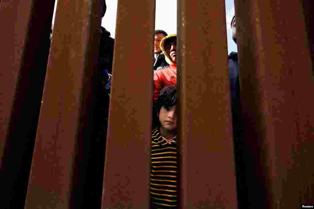 A young boy looks through the border wall as migrants gather between primary and secondary border fences in San Diego near San Diego, California, May 8, 2023.