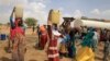FILE - Sudanese refugee women who fled violence in Sudan's Darfur region, carry jerrycans of water as they walk to their shelter near the border between Sudan and Chad in Koufroun, Chad, May 10, 2023.