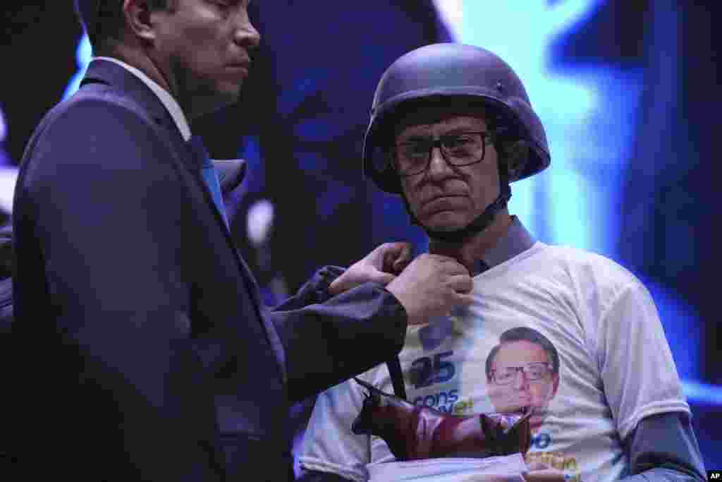 Wearing a bulletproof vest and ballistic helmet, presidential hopeful Christian Zurita, who was named to replace slain candidate Fernando Villavicencio, has his clothing adjusted during his closing campaign rally in Quito, Ecuador, Aug. 17, 2023.