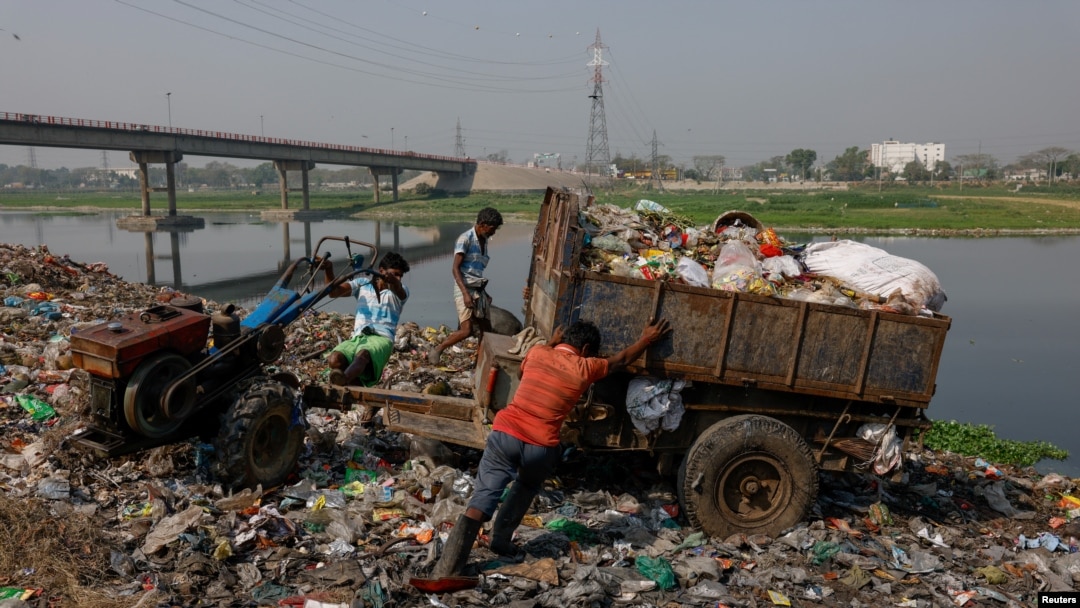FILE - Workers dump waste into a landfill beside Dhaleshwari River, which flows into the Buriganga River, in Savar, near Dhaka, Bangladesh, March 7, 2023. 