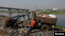 FILE - Workers dump waste into a landfill beside Dhaleshwari River, which flows into the Buriganga River, in Savar, near Dhaka, Bangladesh, March 7, 2023. 