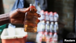 A person holds out a bottle at an informal brewing facility that makes fake whisky, brandy, vodka and other spirits, in Harare