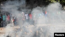 People stand near the remains of alleged gang members after they were set on fire by a crowd in Port-au-Prince, Haiti, April 24, 2023.