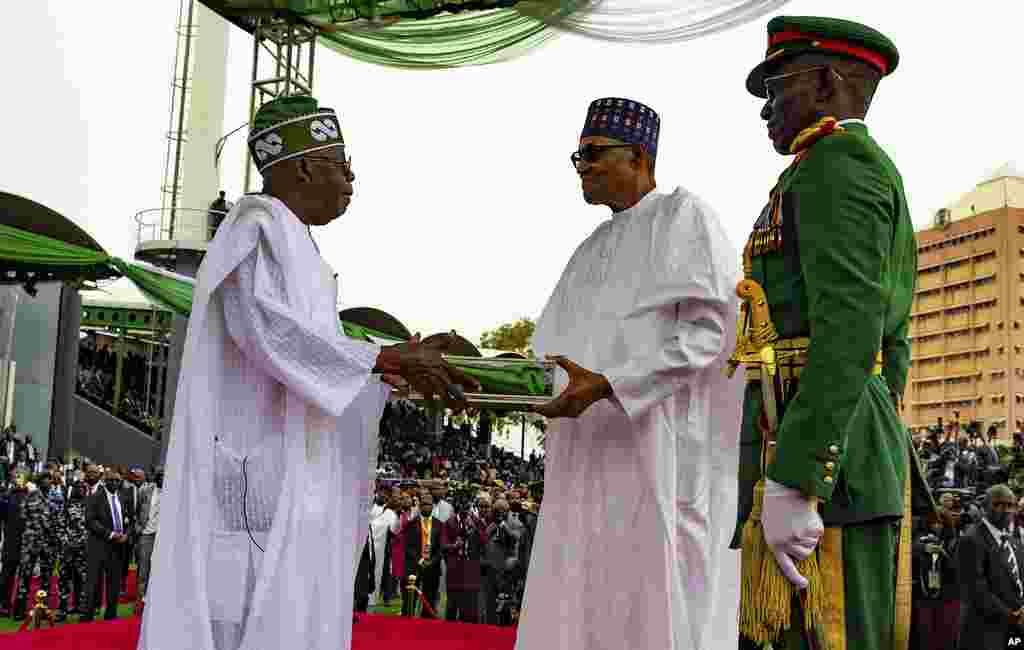 In this photo released by the Nigeria State House, Nigeria's new President Bola Ahmed Tinubu, left, receives Nigeria flags from former Nigerian President Muhammadu Buhari, during the inauguration ceremony in Abuja, Monday, May 29, 2023.