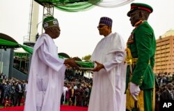 In this photo released by the Nigeria State House, Nigeria's new President Bola Ahmed Tinubu, left, receives Nigeria flags from former Nigerian President Muhammadu Buhari, during the inauguration ceremony in Abuja, May 29, 2023.