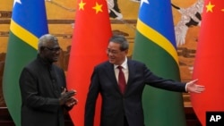 FILE - Chinese Premier Li Qiang, right, shows the way to his Solomon Islands counterpart Manasseh Sogavare after they witnessed signing on agreement for both countries at the Great Hall of the People in Beijing, July 10, 2023.