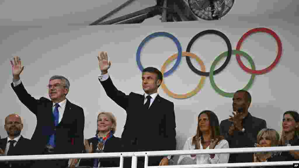 Presiden Prancis Emmanuel Macron, tengah, dan Presiden Komite Olimpiade Internasional (IOC) Thomas Bach, kiri, melambaikan tangan saat mereka tiba untuk menghadiri upacara pembukaan Olimpiade Musim Panas 2024 di Paris, 26 Juli 2024. (Foto:&nbsp;Loic Venance/Pool Photo via AP)