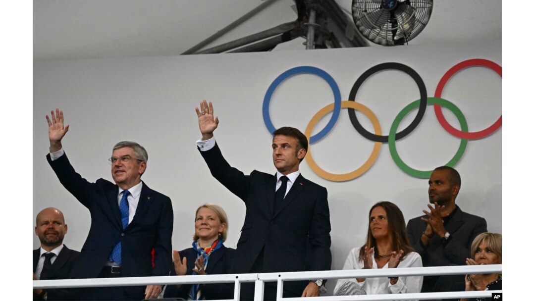 File - Presiden Prancis Emmanuel Macron (tengah) dan Presiden IOC Thomas Bach (kiri) melambaikan tangan saat tiba di podium menjelang upacara pembukaan Olimpiade Musim Panas 2024 di Paris, Prancis, 26 Juli 2024. (Loic Venance/Pool Photo via AP)