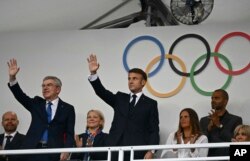 File - Presiden Prancis Emmanuel Macron (tengah) dan Presiden IOC Thomas Bach (kiri) melambaikan tangan saat tiba di podium menjelang upacara pembukaan Olimpiade Musim Panas 2024 di Paris, Prancis, 26 Juli 2024. (Loic Venance/Pool Photo via AP)