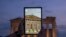 FILE - A man holds up a tablet showing a digitally overlaid  virtual reconstruction of the ancient Parthenon temple, at the Acropolis Hill in Athens, Greece, June 13, 2023. 