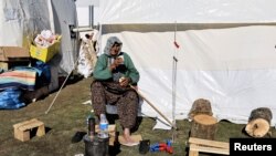 A woman eats food outside her tent at an athletic track that is serving as a camp for survivors, in the aftermath of a deadly earthquake, in Adiyaman, Turkey, Feb. 17, 2023.