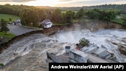 This drone photo provided by AW Aerial shows a home as it teeters before partially collapsing into the Blue Earth River at the Rapidan Dam in Rapidan, Minnesota, June 25, 2024. 