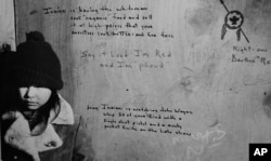 FILE - A child stands in front of sayings written on a wall during the occupation of Wounded Knee, S.D., by members of the American Indian Movement in 1973.