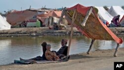 Korban banjir berlindung di bawah bayang-bayang dipan di pinggir jalan Jaffarabad, sebuah distrik di provinsi Baluchistan barat daya, Pakistan, Senin, 19 September 2022. (AP/Zahid Hussain )