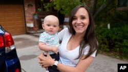 Carrie Martin-Haley menggendong anaknya di luar rumahnya di Greenwood Village, Colorado, pada 10 Mei 2024. Colorado mulai memberlakukan cuti kesehatan dan cuti keluarga berbayar awal tahun ini. (Foto: AP/David Zalubowski)