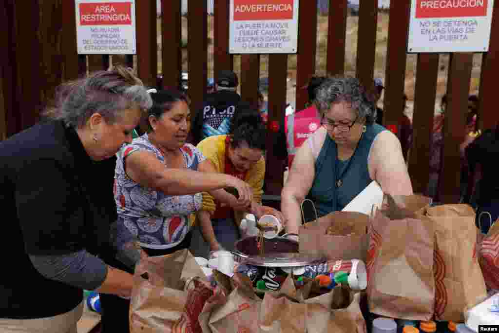 Voluntarios ayudan a alimentar a los migrantes, que se han reunido entre las vallas fronterizas primarias y secundarias, entre Estados Unidos y México,