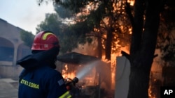 A firefighter works to extinguish the flames at a burning house in northern Athens, Aug. 12, 2024, as hundreds of firefighters tackle a major wildfire. Dry pine forests and strong winds have aided the fire, making it difficult for firefighters to get the blaze under control.  