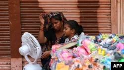 People sit in front of a table fan to cool off on a hot summer afternoon in Varanasi, India, on May 29, 2024.