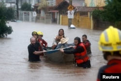 FILE - Rescue workers evacuate a family with a pet from a flooded area in the Cavalhada neighborhood in Porto Alegre, Brazil, May 23, 2024.