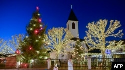 ILUSTRASI - Pengunjung berjalan di depan pepohonan yang berhiaskan lampu-lampu dan dekorasi Natal di gereja Katolik setempat pada malam perayaan Natal di desa Petrushan, dekat kota Gjakova, Kosovo, 18 Desember 2023. (Foto oleh Armend NIMANI / AFP)