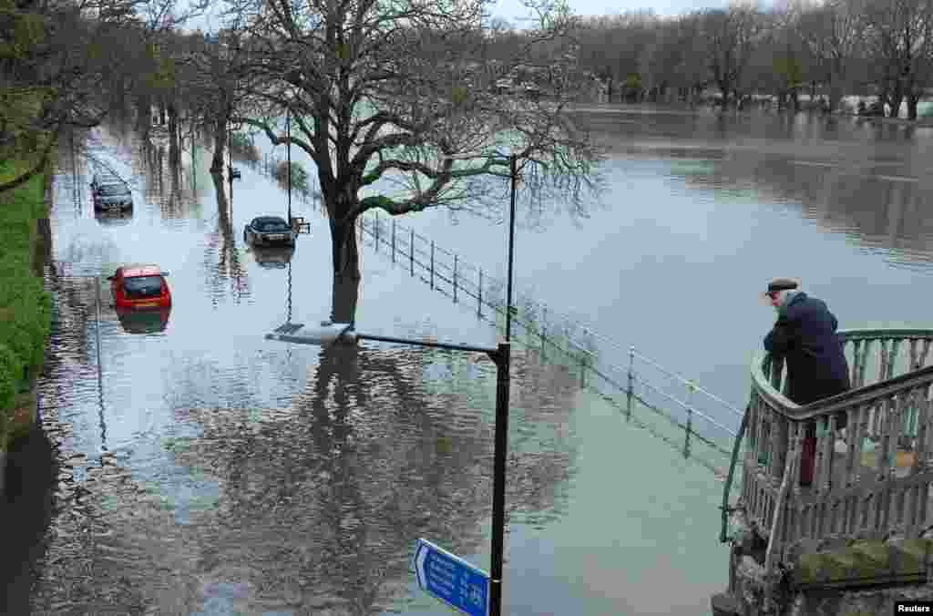 A man looks towards partially submerged cars as the River Thames bursts its banks at high tide, in Richmond in London, March 12, 2024. 