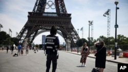 A security officer watches people taken photographs in front of the Eiffel Tower at the 2024 Summer Olympics in Paris, July 20, 2024.